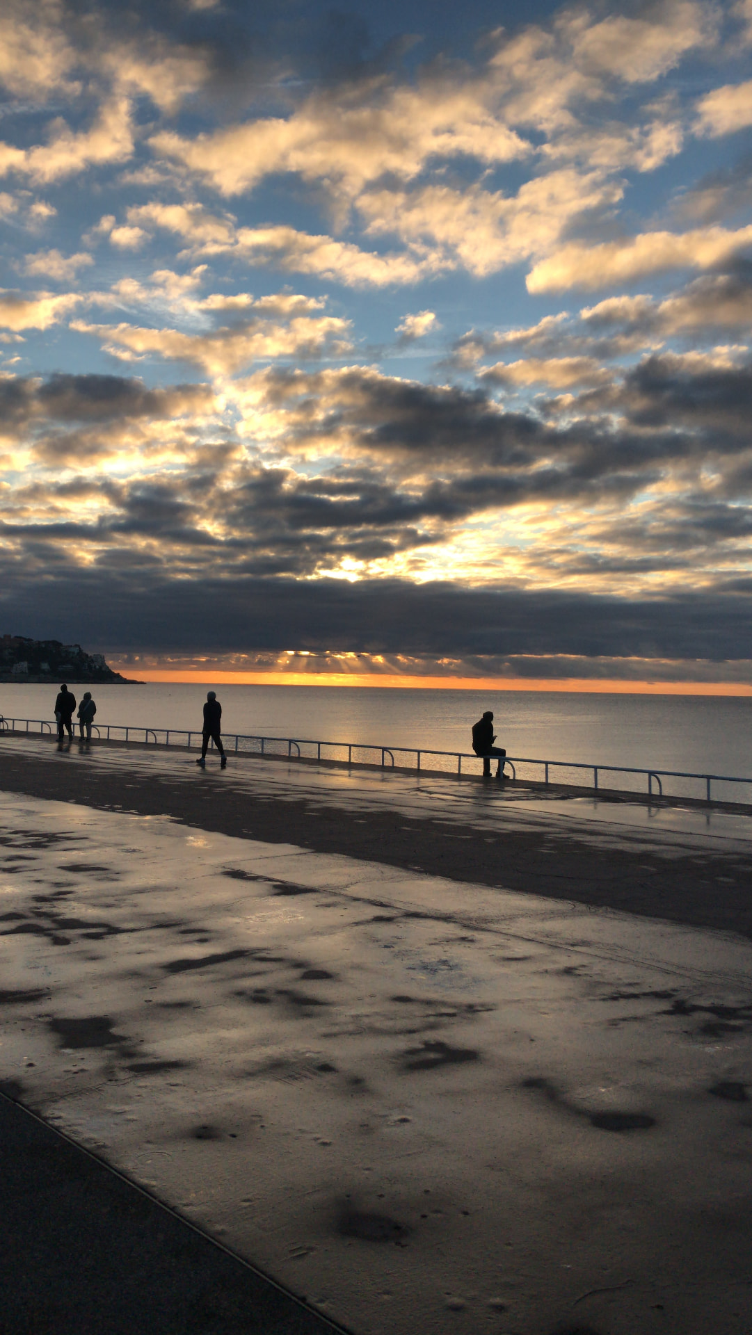 A seafront promenade at dusk, figures silhouetted against the last light over the water.